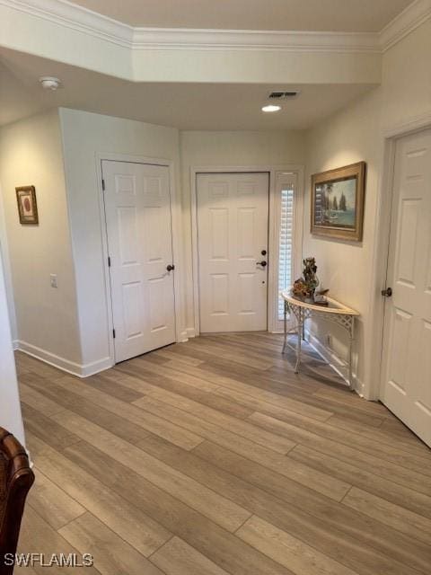 hallway with baseboards, light wood finished floors, visible vents, and crown molding