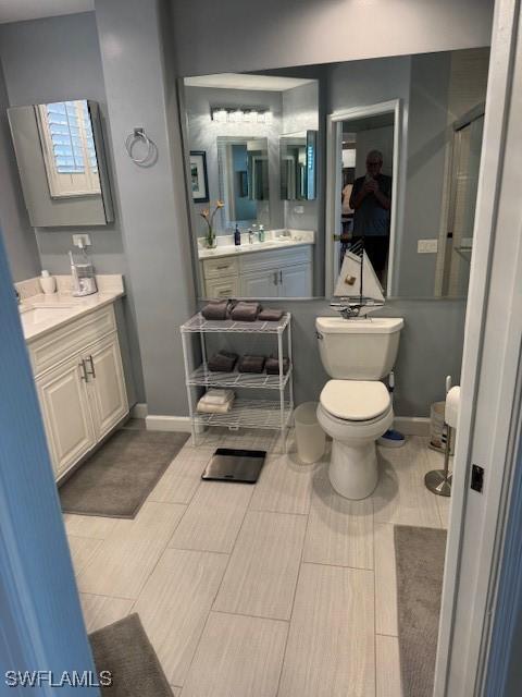 full bathroom featuring baseboards, two vanities, toilet, and a shower stall