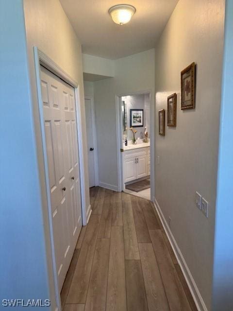 hallway featuring a sink, baseboards, and wood finished floors