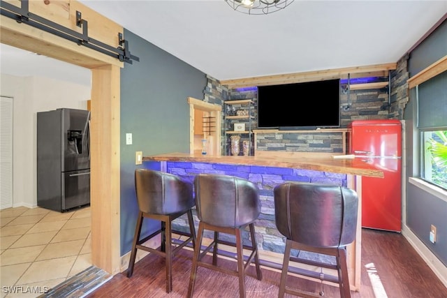 bar featuring a barn door, an accent wall, refrigerator with ice dispenser, baseboards, and a dry bar