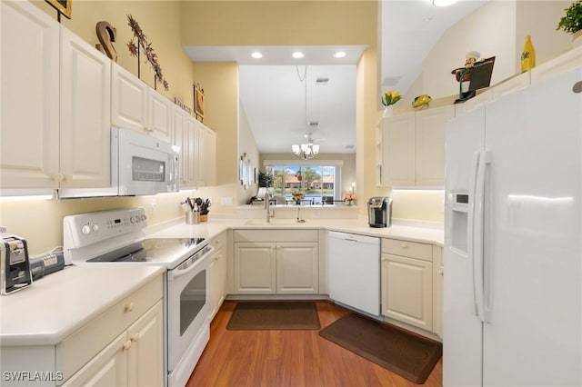 kitchen with wood finished floors, a sink, white appliances, an inviting chandelier, and light countertops