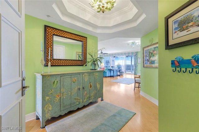 hallway with a raised ceiling, crown molding, wood finished floors, and baseboards