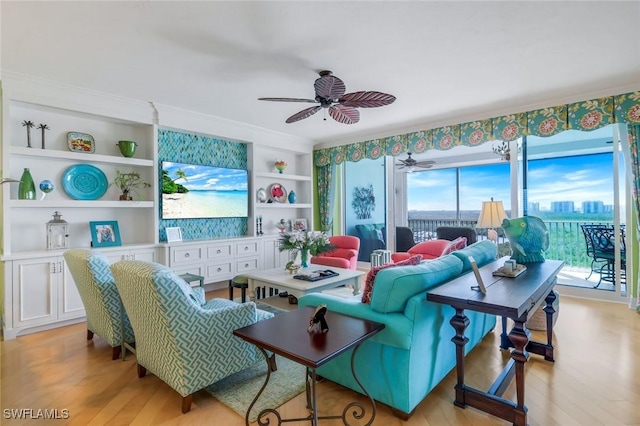 living room featuring built in shelves, light wood-style floors, ornamental molding, and a ceiling fan