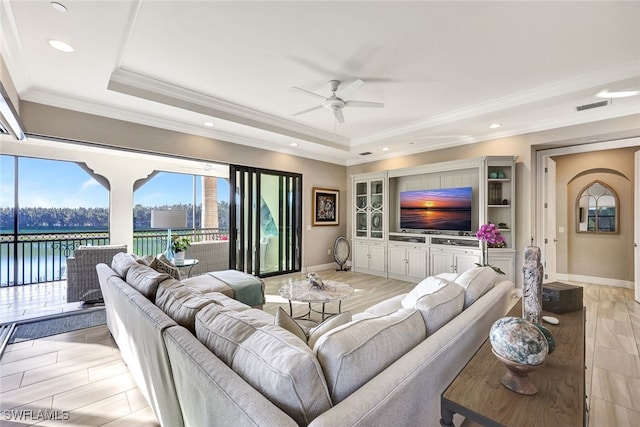 living area with light wood-style flooring, a water view, visible vents, a raised ceiling, and crown molding