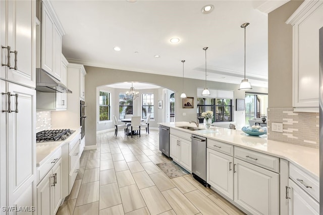 kitchen with recessed lighting, arched walkways, appliances with stainless steel finishes, under cabinet range hood, and a notable chandelier