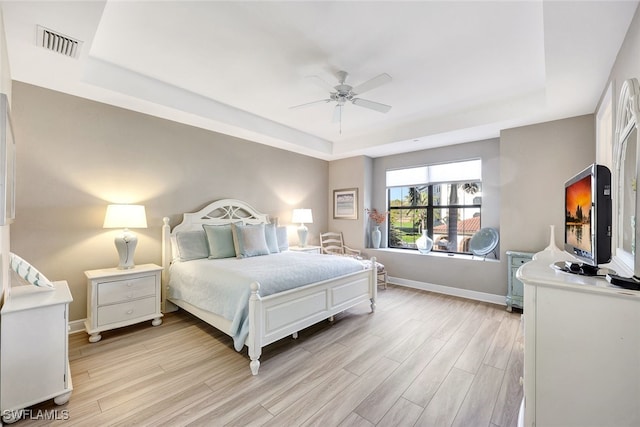 bedroom featuring visible vents, ceiling fan, a tray ceiling, baseboards, and light wood finished floors