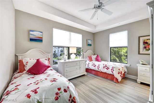 bedroom featuring baseboards, a ceiling fan, light wood-style floors, and a tray ceiling