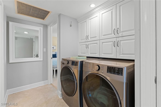 washroom with light tile patterned floors, visible vents, cabinet space, washer and dryer, and baseboards