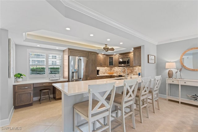 kitchen featuring a breakfast bar area, a raised ceiling, backsplash, appliances with stainless steel finishes, and a sink