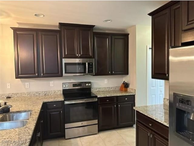 kitchen featuring light tile patterned floors, light stone counters, stainless steel appliances, dark brown cabinets, and a sink