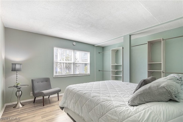 bedroom with a textured ceiling, baseboards, and wood finished floors