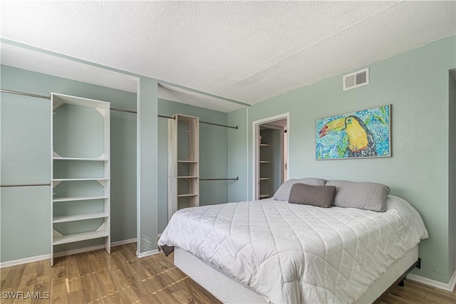 bedroom with a textured ceiling, wood finished floors, visible vents, and baseboards