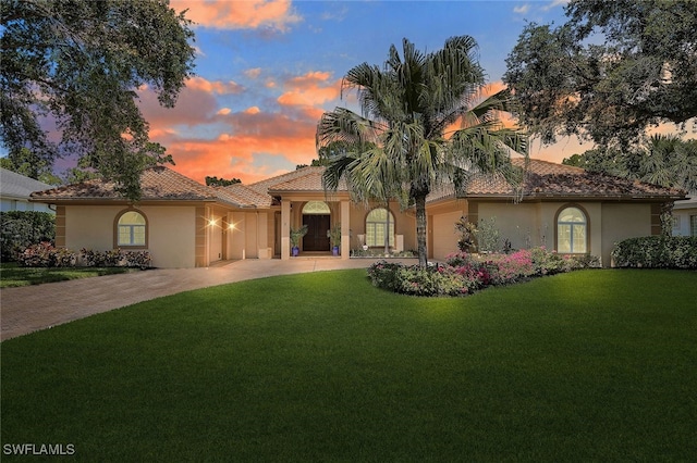 mediterranean / spanish house with a garage, stucco siding, decorative driveway, and a yard