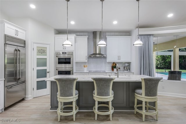 3311 Creekview Dr, Bonita Springs, FL 34134 - kitchen featuring appliances with stainless steel finishes, wall chimney range hood, tasteful backsplash, white cabinetry, and light wood-style floors