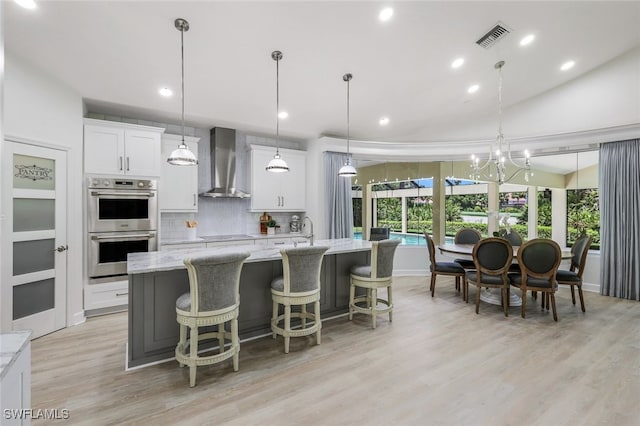 3311 Creekview Dr, Bonita Springs, FL 34134 - kitchen featuring wall chimney range hood, double oven, an island with sink, light wood finished floors, and white cabinets