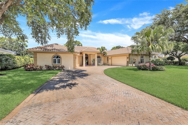 mediterranean / spanish house featuring stucco siding, a tile roof, an attached garage, decorative driveway, and a front yard