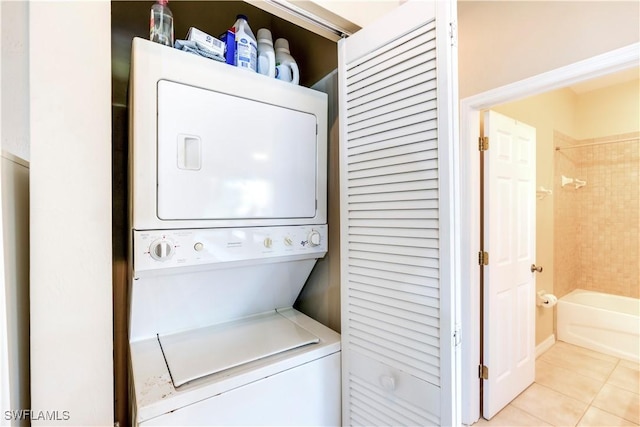 clothes washing area featuring light tile patterned floors, stacked washer / drying machine, and laundry area