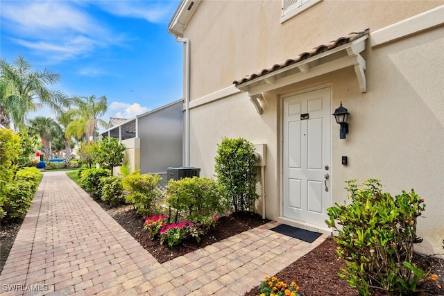 property entrance with stucco siding, cooling unit, and a tile roof