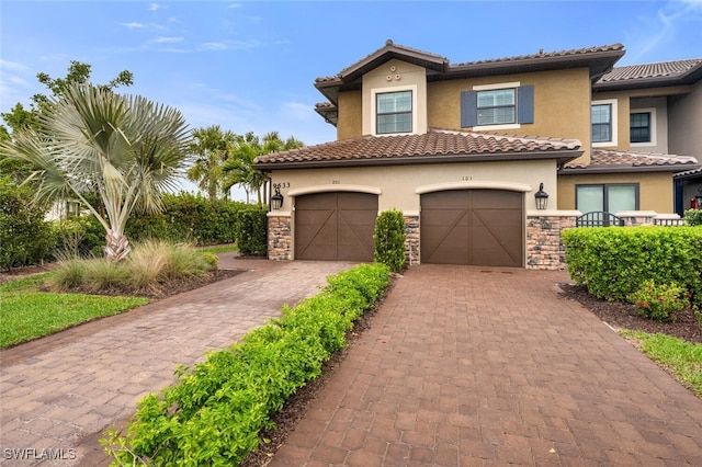 mediterranean / spanish house featuring stucco siding, decorative driveway, stone siding, an attached garage, and a tiled roof