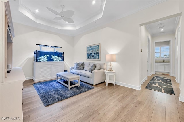 living area featuring a raised ceiling, light wood-style floors, and ornamental molding