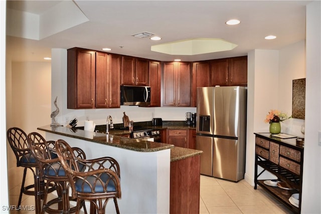 kitchen featuring stainless steel appliances, recessed lighting, light tile patterned flooring, dark stone countertops, and a peninsula