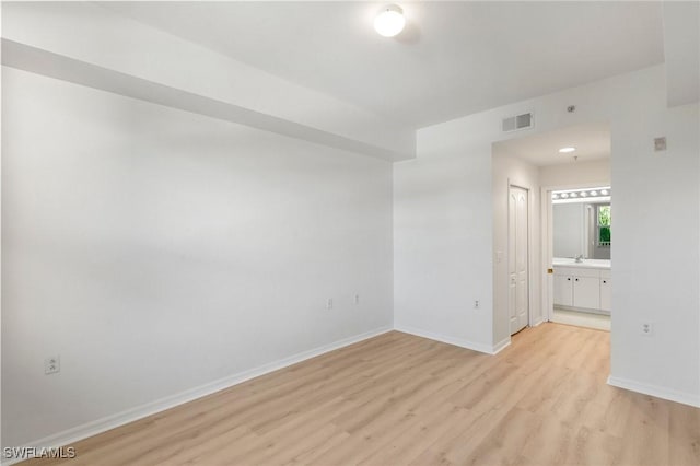 unfurnished room featuring visible vents, light wood-style floors, baseboards, and a sink