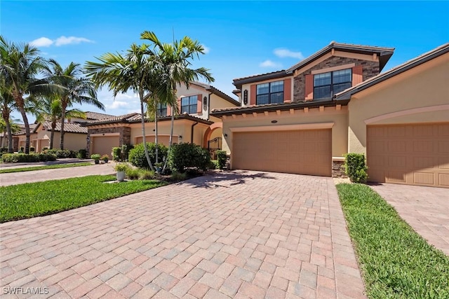 mediterranean / spanish-style house with a tiled roof, stucco siding, decorative driveway, a garage, and stone siding