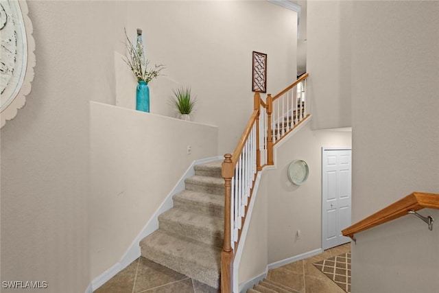 staircase with tile patterned floors, baseboards, and a high ceiling