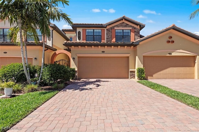 mediterranean / spanish house featuring stucco siding, stone siding, a tile roof, and decorative driveway