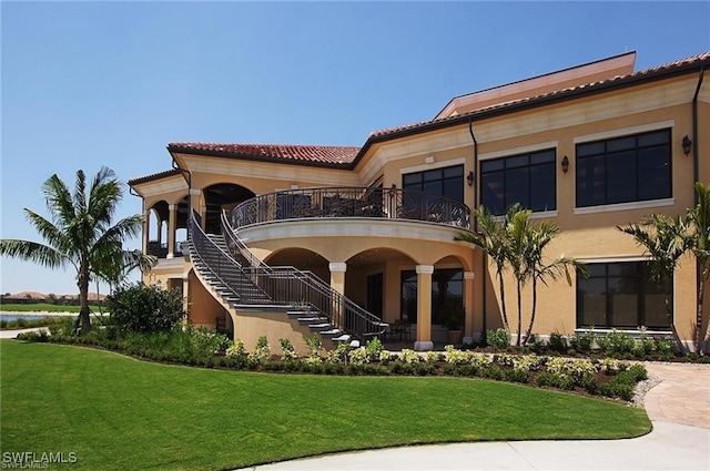 back of house featuring stucco siding, a lawn, stairs, and a tiled roof