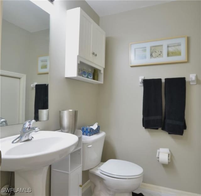 half bath with toilet, a sink, and baseboards