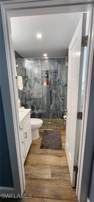 full bath featuring a tile shower, toilet, wood finished floors, and vanity