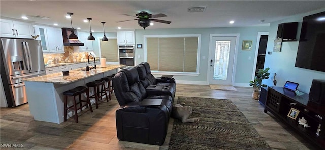 kitchen featuring a breakfast bar, stainless steel appliances, open floor plan, white cabinetry, and wall chimney exhaust hood