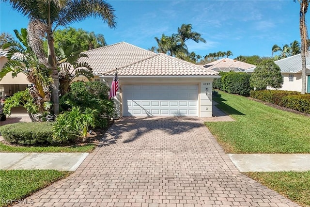 view of front of house featuring an attached garage, a tile roof, decorative driveway, and a front yard