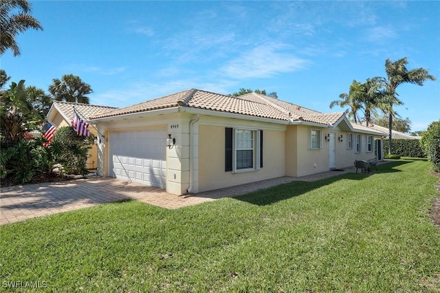 view of side of property featuring a garage, a tiled roof, a yard, driveway, and stucco siding