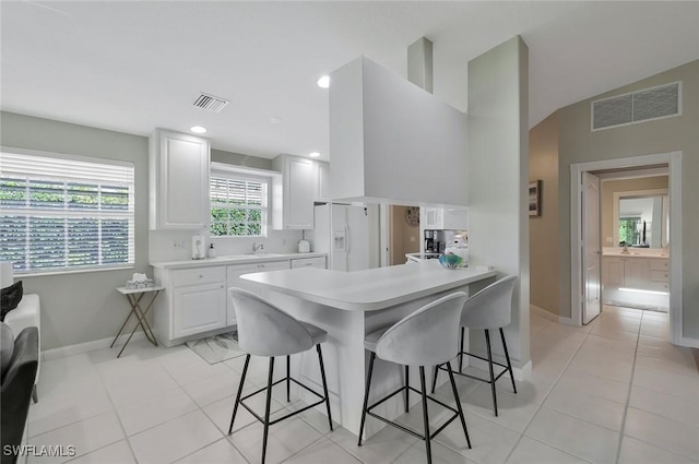 kitchen with white fridge with ice dispenser, a breakfast bar, and visible vents