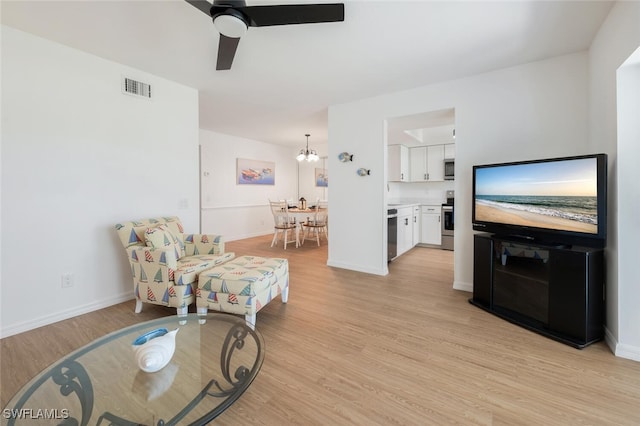 living area with light wood-type flooring, baseboards, visible vents, and ceiling fan with notable chandelier