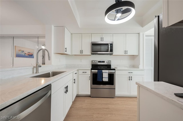 kitchen featuring light stone counters, light wood finished floors, stainless steel appliances, white cabinetry, and a sink