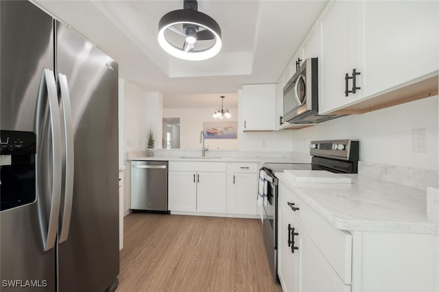 kitchen with stainless steel appliances, white cabinetry, a sink, and light wood-style flooring