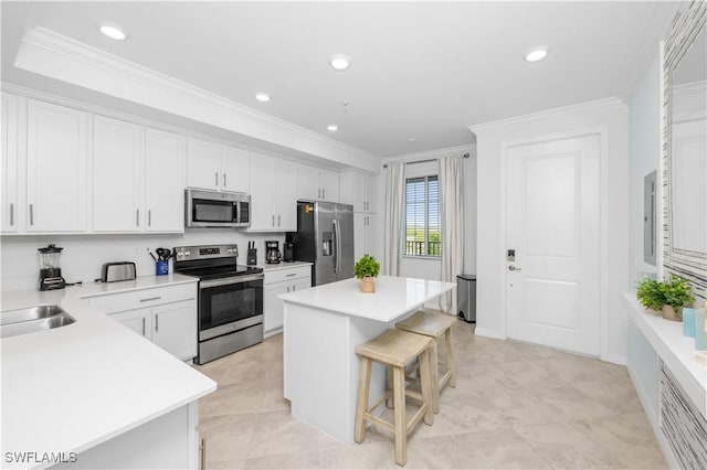 kitchen with white cabinets, a center island, ornamental molding, appliances with stainless steel finishes, and a breakfast bar