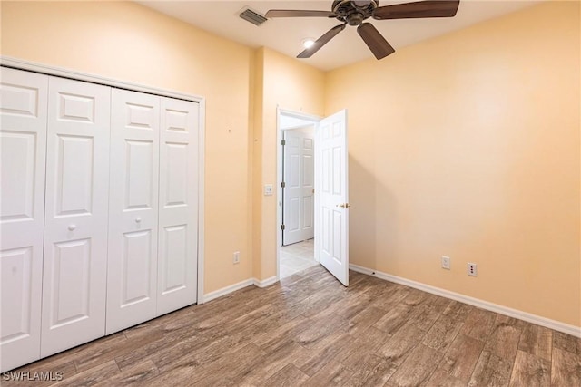 unfurnished bedroom with wood finished floors, visible vents, a closet, and baseboards