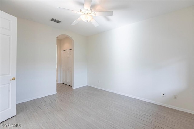 spare room with light wood finished floors, visible vents, baseboards, ceiling fan, and arched walkways