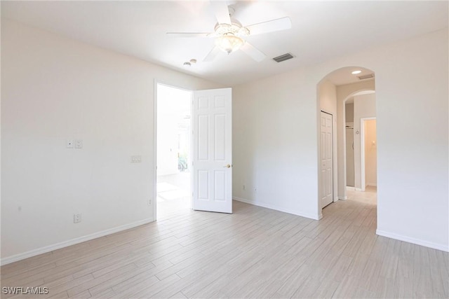 spare room featuring visible vents, arched walkways, light wood finished floors, baseboards, and ceiling fan