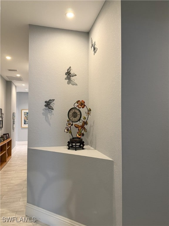 hallway with baseboards, a textured wall, recessed lighting, and light wood-style floors