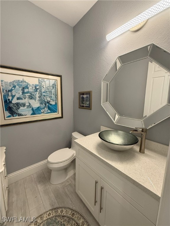 bathroom featuring toilet, wood finished floors, vanity, and baseboards