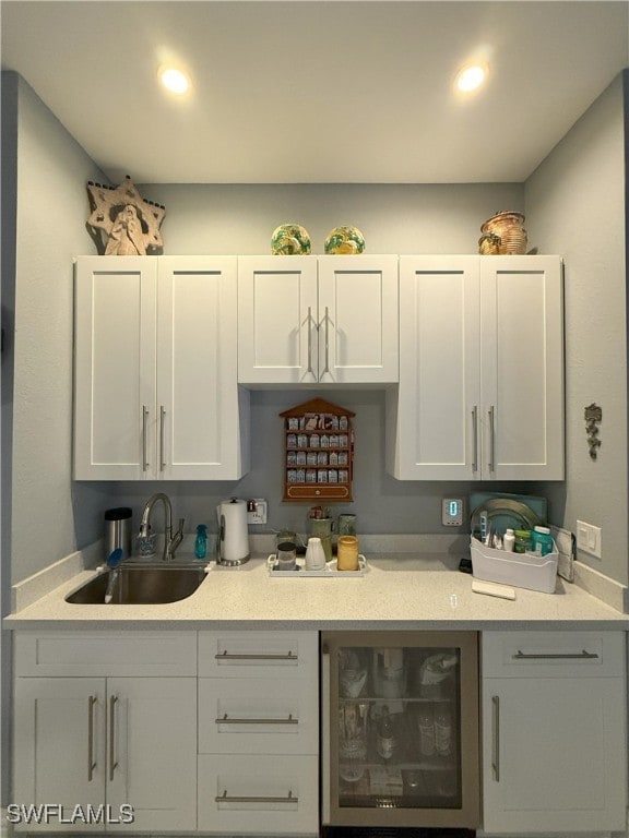 kitchen with wine cooler, recessed lighting, light countertops, white cabinets, and a sink