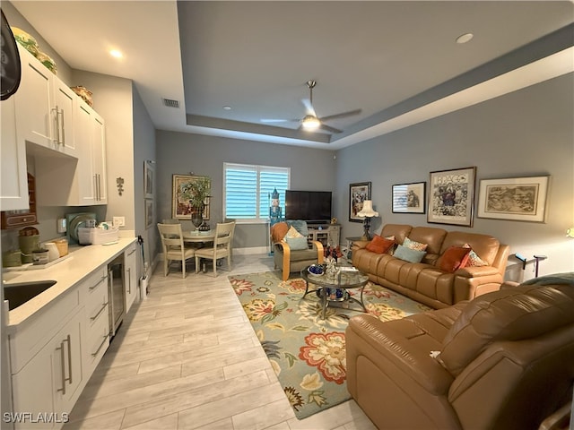 living area featuring visible vents, baseboards, light wood-style flooring, ceiling fan, and a tray ceiling