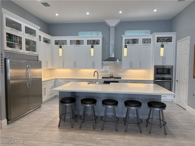 kitchen featuring built in appliances, a sink, visible vents, wall chimney exhaust hood, and tasteful backsplash