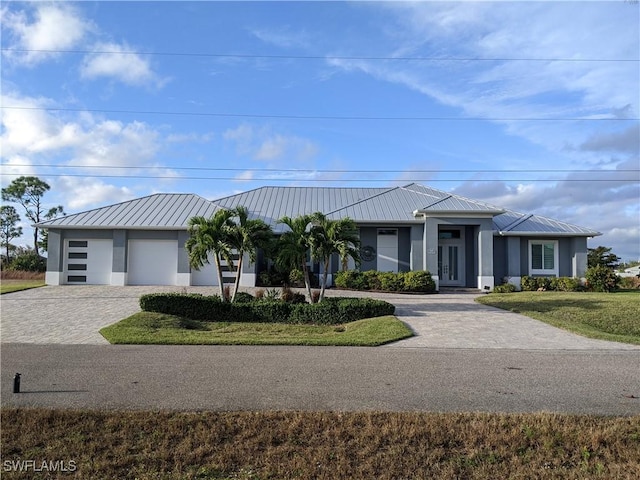 view of front facade with metal roof, a garage, decorative driveway, stucco siding, and a standing seam roof