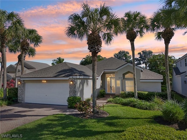 view of front of house with a garage, roof with shingles, decorative driveway, a front yard, and stucco siding